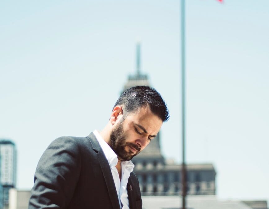 Man in a suit checking phone outdoors with Canadian flag, symbolizing LMIA Canadian work opportunities.
