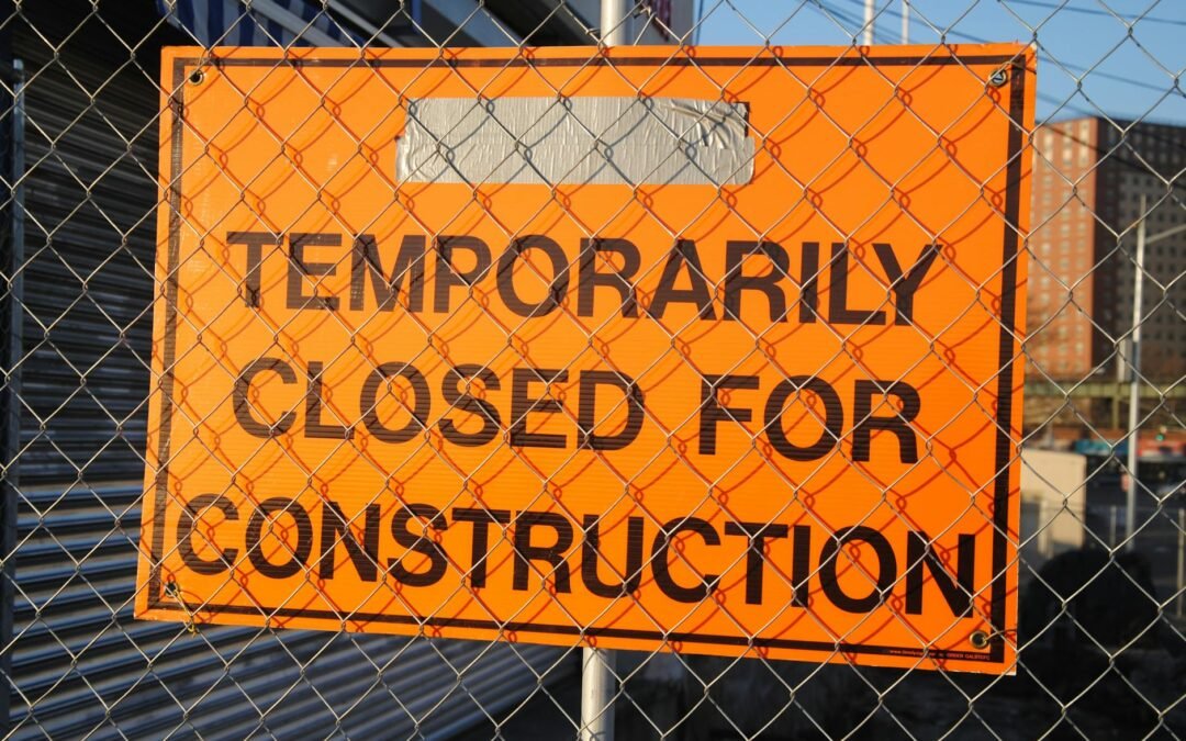 Orange sign stating "Temporarily Closed for Construction" on a fenced site.