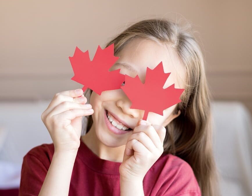 Child holding red maple leaf cutouts, symbolizing Canadian pride and citizenship.