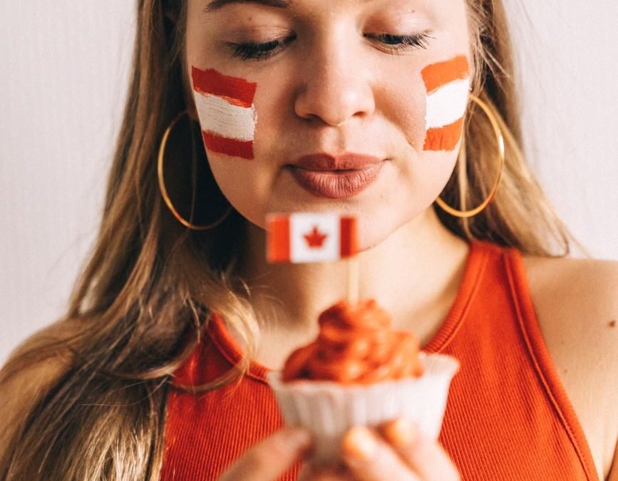 Woman with Canadian flag-themed face paint holding dessert, symbolizing Canadian culture and tech immigration.