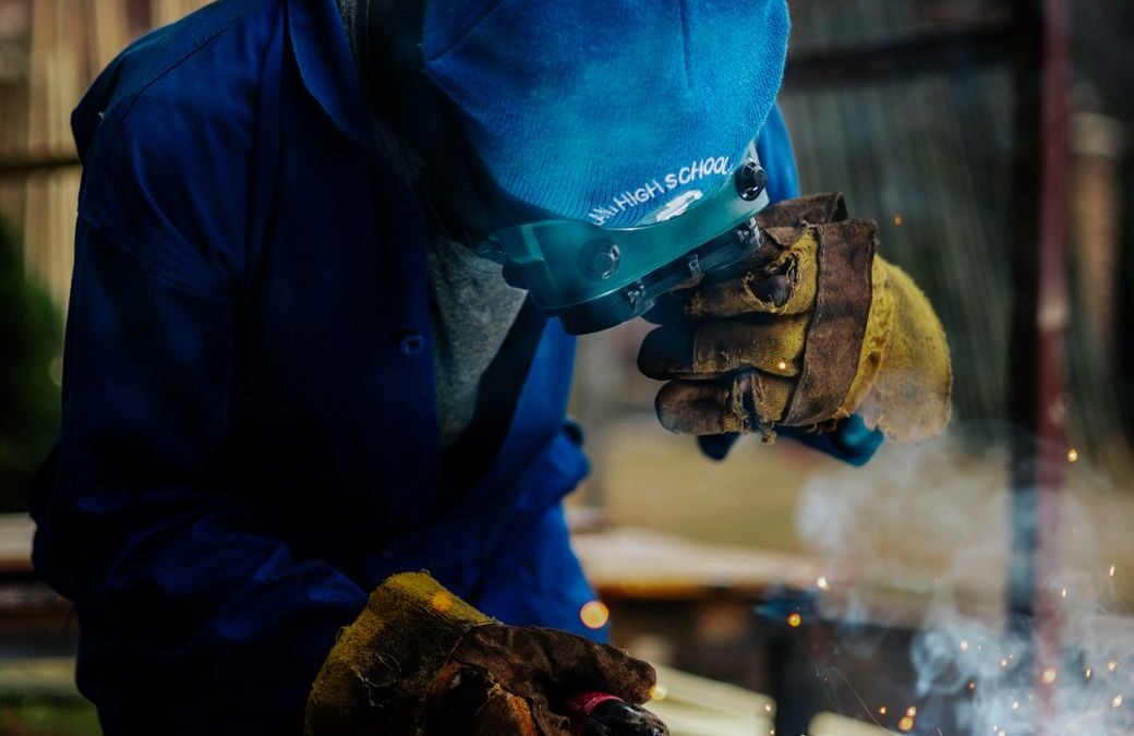 Young skilled worker welding in a rural setting, showcasing craftsmanship and vocational training.